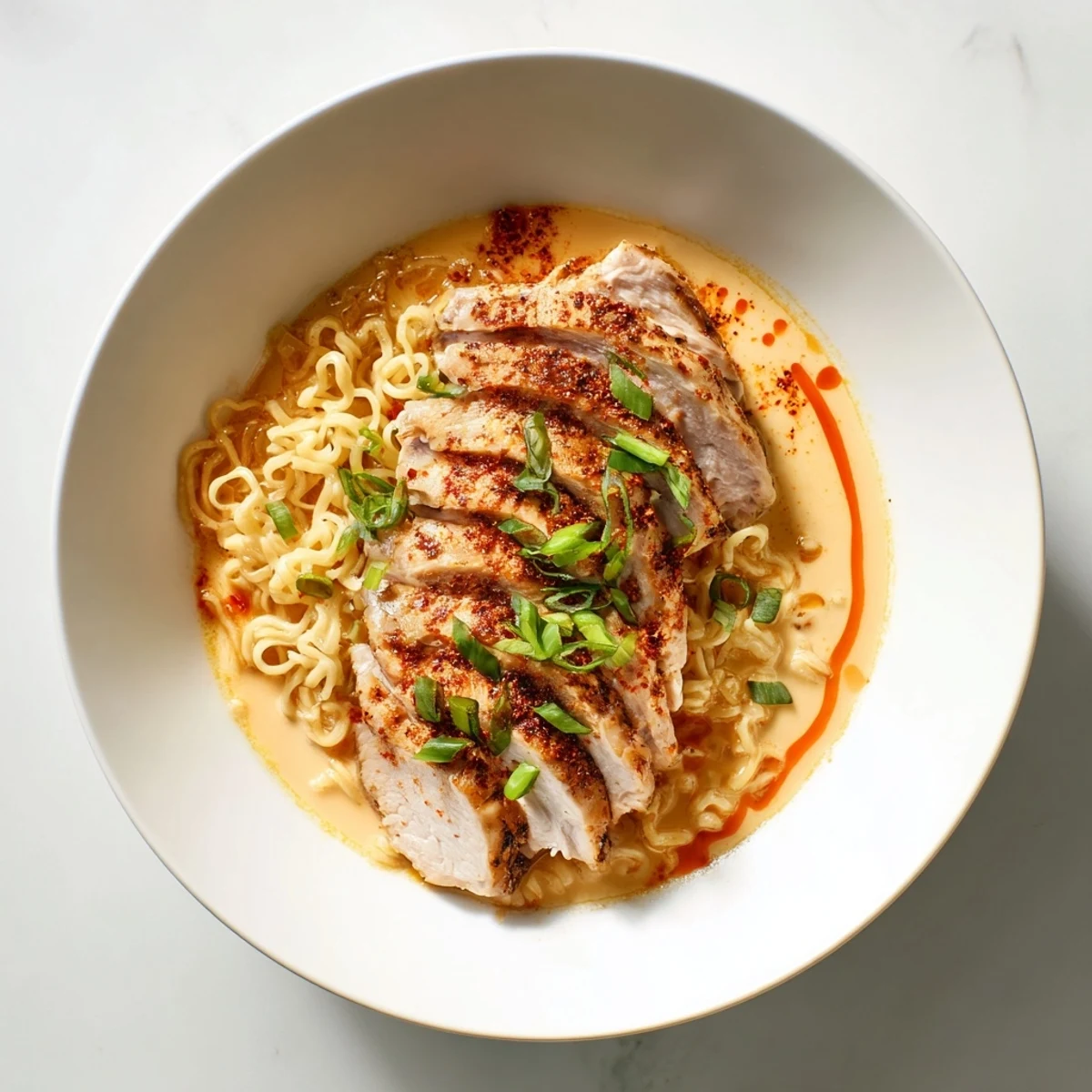 Steaming bowl of Fiery Chicken Ramen showcasing tender chicken slices and vibrant green onions floating in a rich broth.