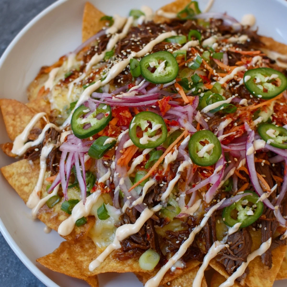 A close-up of Korean BBQ Nachos with melted cheese, savory beef, and fresh vegetable toppings.
