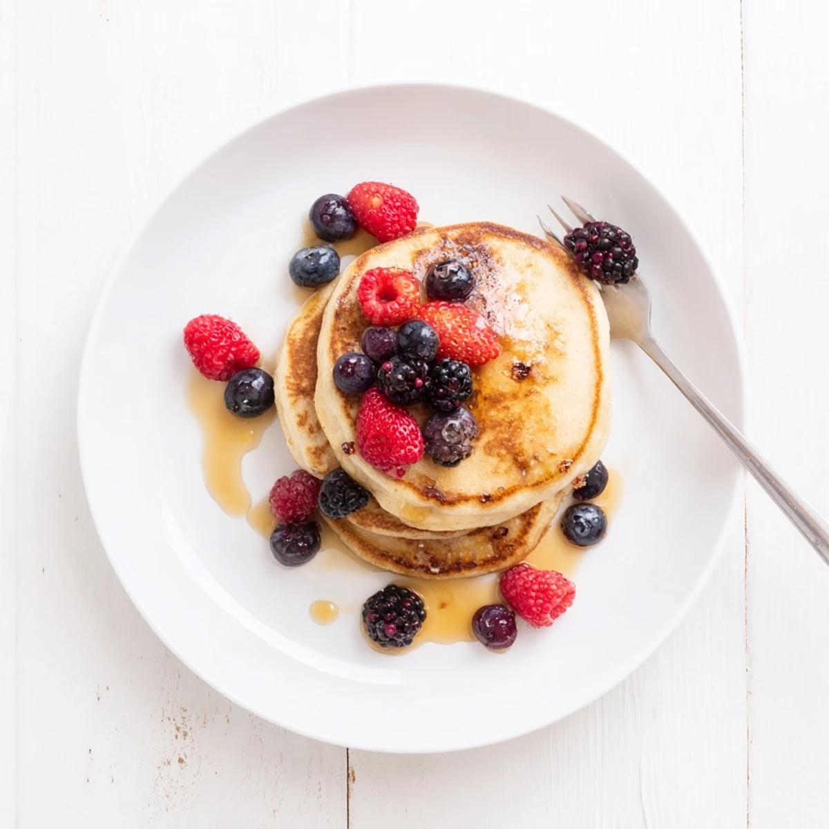 Golden-brown banana pancakes stacked high on a white plate, topped with fresh berries and a drizzle of maple syrup.