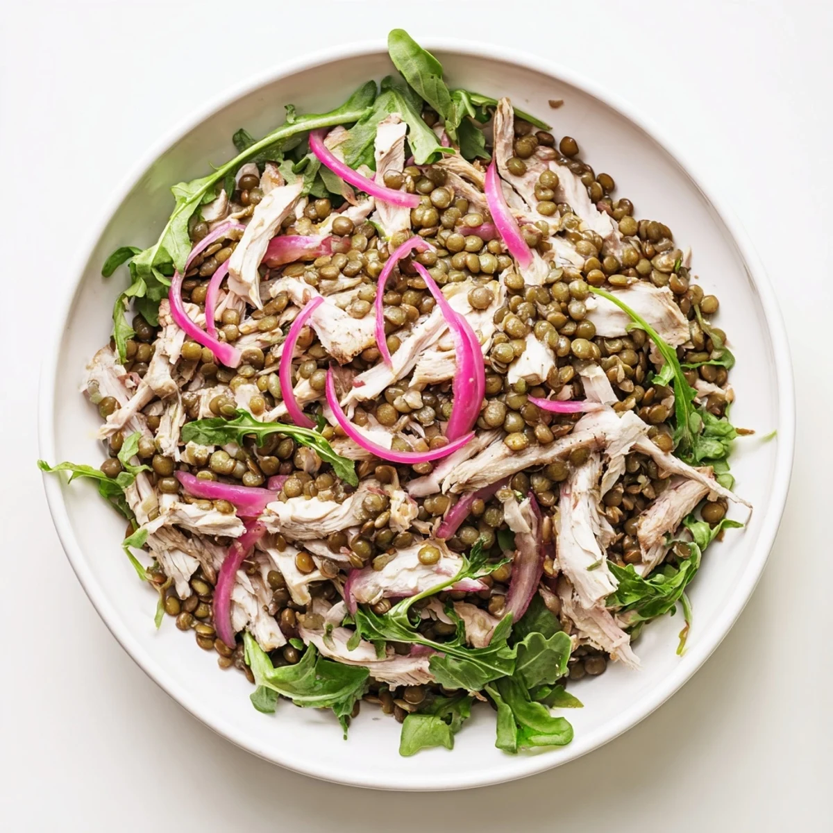 A close-up of the Lentil & Chicken Spring Salad shows tender lentils, juicy shredded chicken, and fresh arugula tossed in a mustard dressing with pickled onions.