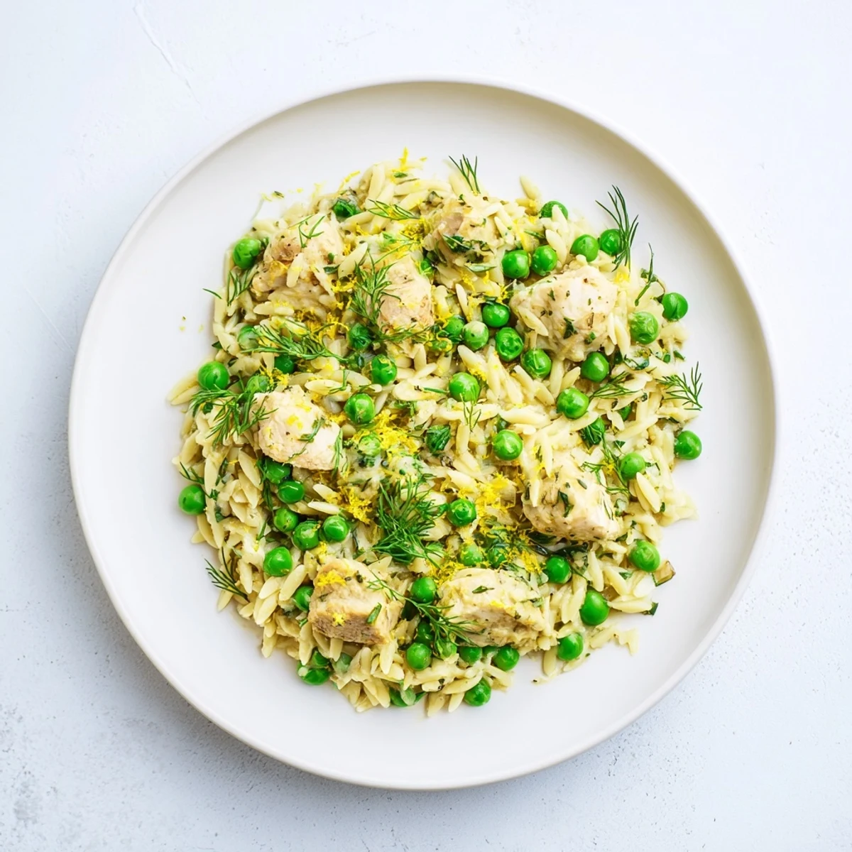 Golden-brown chicken pieces, orzo pasta, and bright green peas simmer in a zesty lemon herb sauce in a single skillet.