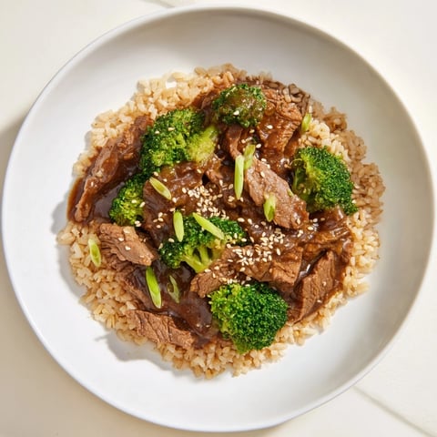 Tender Slow-Cooker Beef & Broccoli: savory beef and broccoli, served atop fluffy brown rice, and garnished with fresh scallions.