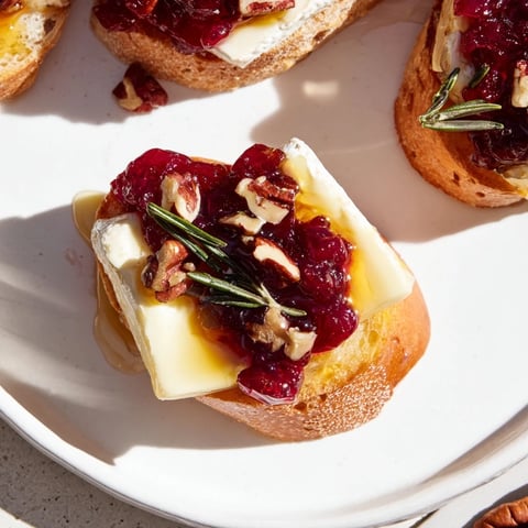 Golden, toasted Quick Cranberry Brie Crostini topped with vibrant cranberry sauce and rosemary.