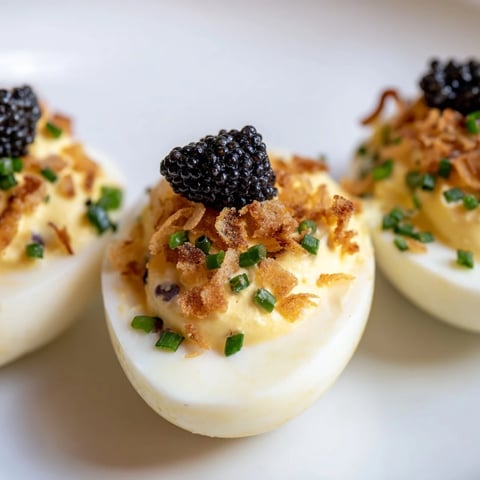 Elegant deviled eggs topped with glistening caviar and crunchy shallots, a gourmet appetizer.