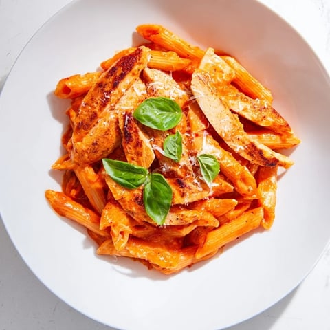 A close-up of Spicy Tomato Chicken Pasta with seared chicken strips nestled in penne coated in a vibrant chili tomato sauce.  