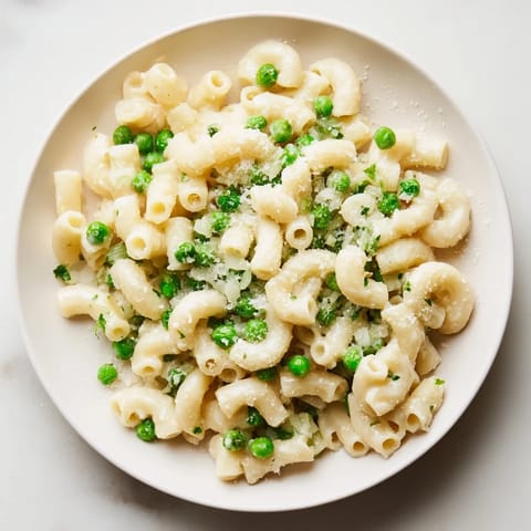A close-up of buttery Macaroni & Peas, with visible peas and Parmesan topping.
