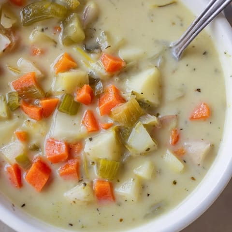 A close-up of thick, creamy dill pickle soup boasting chunks of fresh pickles and herbs ready to serve.