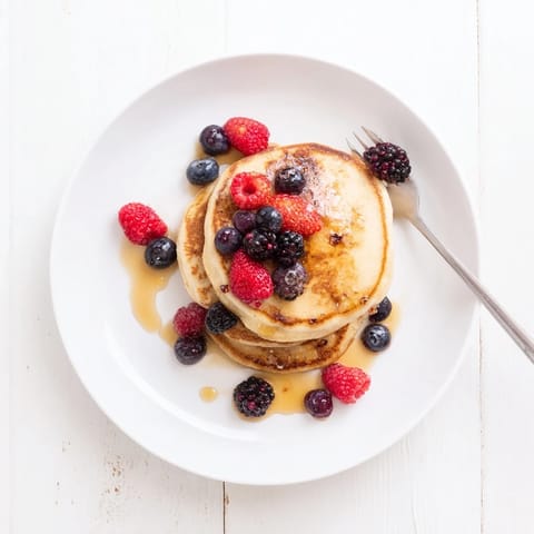 Golden-brown banana pancakes stacked high on a white plate, topped with fresh berries and a drizzle of maple syrup.