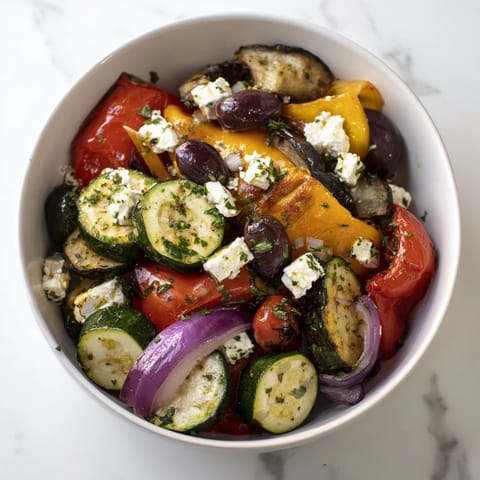 A close-up of golden, caramelized vegetables topped with crumbled feta, fresh parsley, and a bright lemon-oregano dressing.  