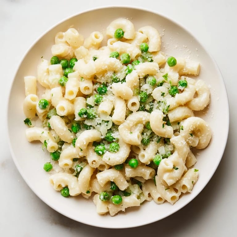 A close-up of buttery Macaroni & Peas, with visible peas and Parmesan topping.