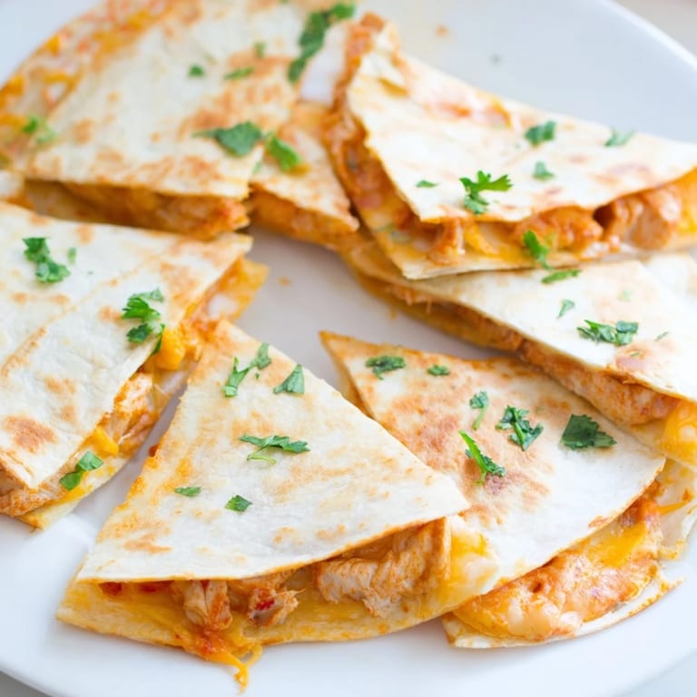 A close-up of a warm Butter Chicken Quesadilla, showing spiced chicken and cheese filling.