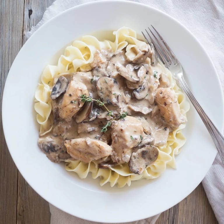 Steaming plate of Chicken and Mushroom Stroganoff featuring tender meat, earthy mushrooms, and a velvety sauce garnished with parsley.