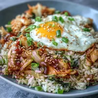 Spicy kimchi cabbage fried rice with a golden fried egg and toasted sesame seeds, perfect for a quick and flavorful meal.